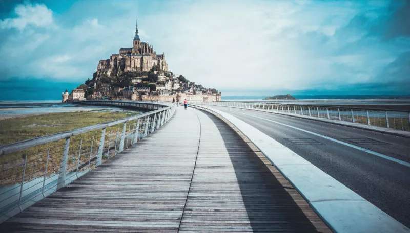 View of Mont-Saint Michel from a distance with walkway in centre image. Just one of many amazing cities to explore in Normandy