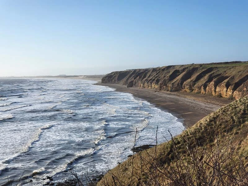 Durham Heritage Coast. Blue sea with white-crested waves washing on a pebble beach set against a curved coastline. Just one of many things to do in Durham for couples