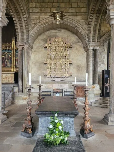 The black topped Shrine of St Bede located in the lower half of photo with gold Latin text against the rear wall. 