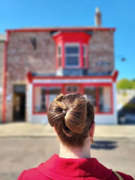 Photo of Roma, taken from behind her, showing the new Bow hairstyle. Roma is in focus, Elizabeth's Hairdressing building in blurred background