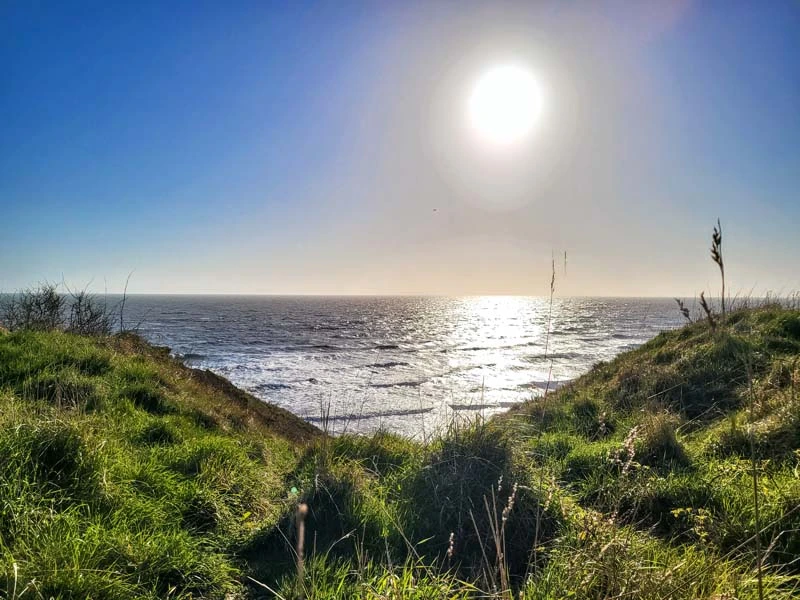 Sea views in the middle of the photo, green coastline in the lower half, and sun in the top half. Just one of many things to do in Durham for couples