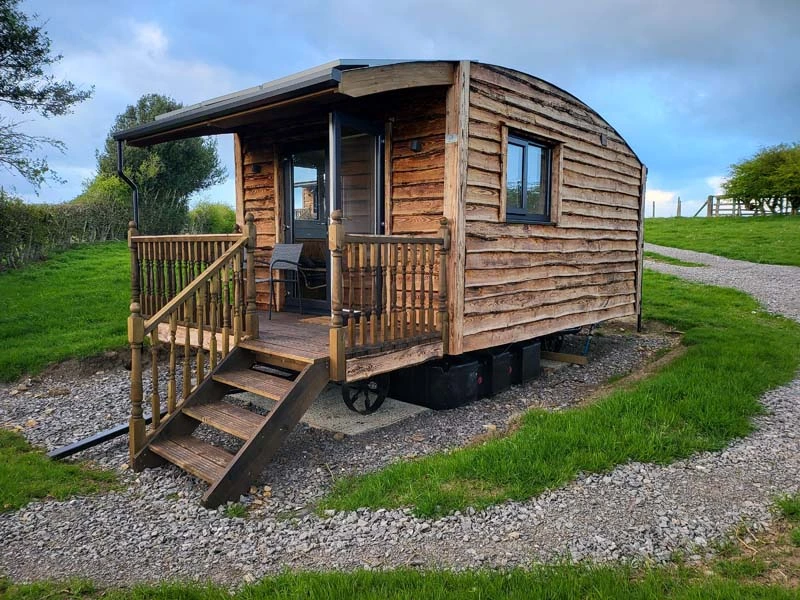 Glamping at Teesdale Cheesemaker's. Modern wooden Shepherd's Hut. The cabin has 4 steps to the interior, deck is visible and 2 main windows. 