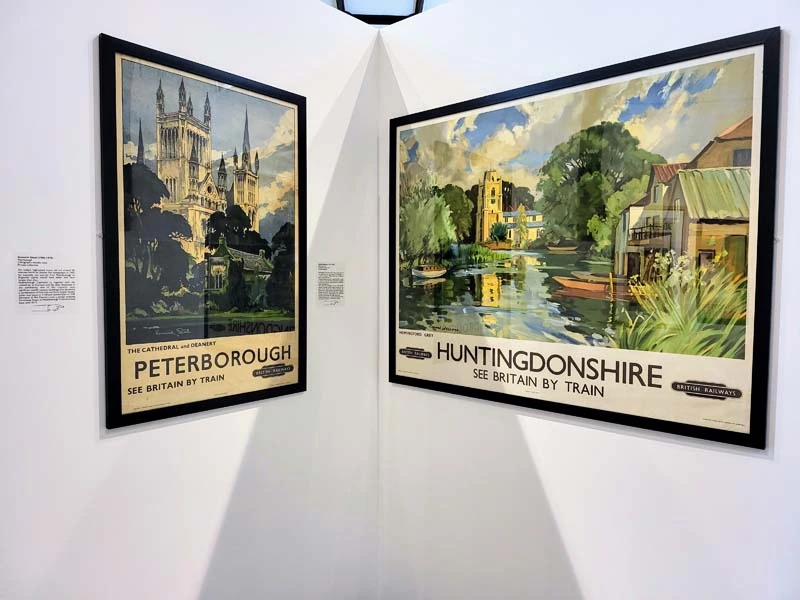 Interior photo from temporary exhibit. Framed railway posters hanging on white wall. The posters show destination names - Peterborough and Huntingdonshire. Just one of many things to do in Durham for couples