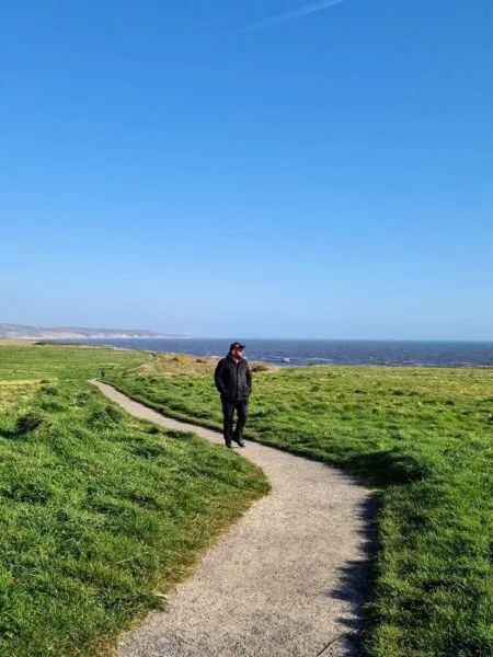 Russell walking along coastal footpath, surrounded by green grass, and a bright blue sky