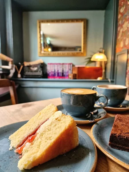 A slice of cake on a plate with artwork in background at Lutt and Turner in Malton, North York Moors 